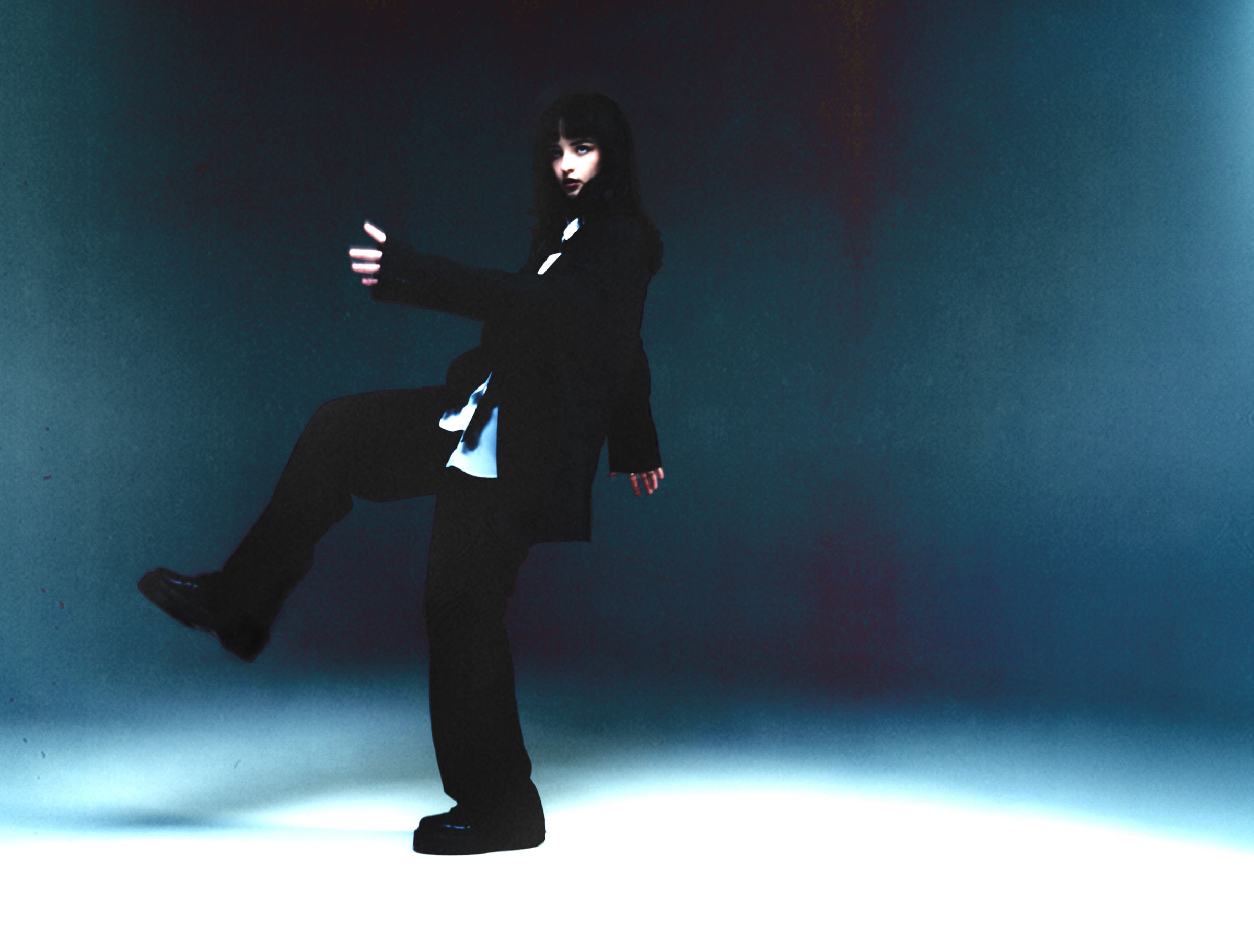 Irina Dengina in a black suit, mid-kick against a blue studio backdrop